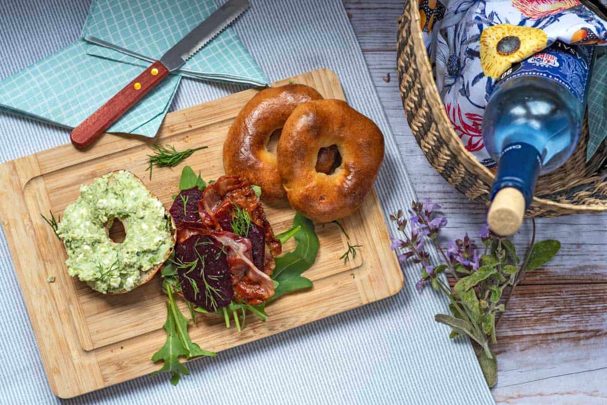 Open bagel with pea puree spread on one side and beets and bacon on the bottom half. 