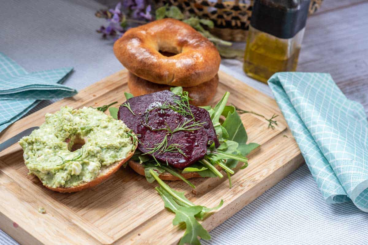 open bagel with roasted beets and salad and pea puree on the top half. 