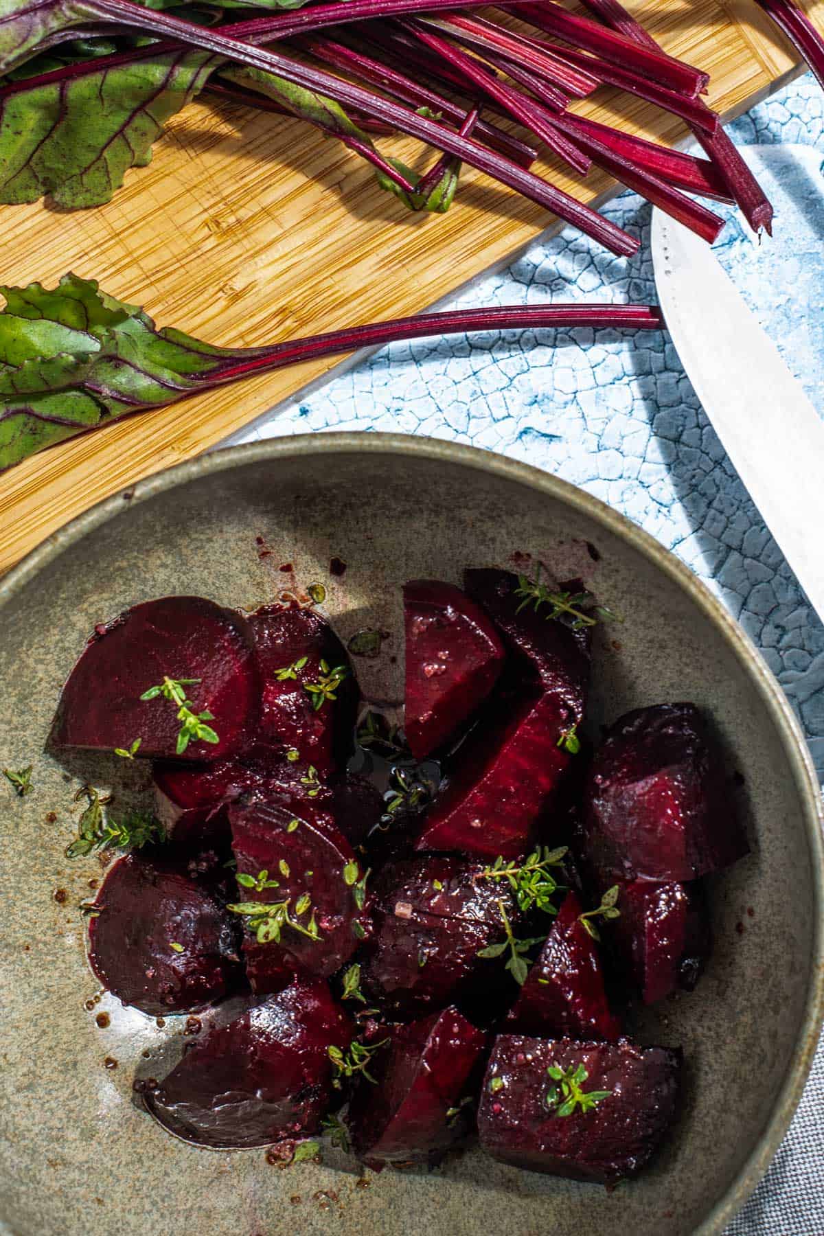 A bowl of diced beets alongside fresh beet greens on a wooden board.