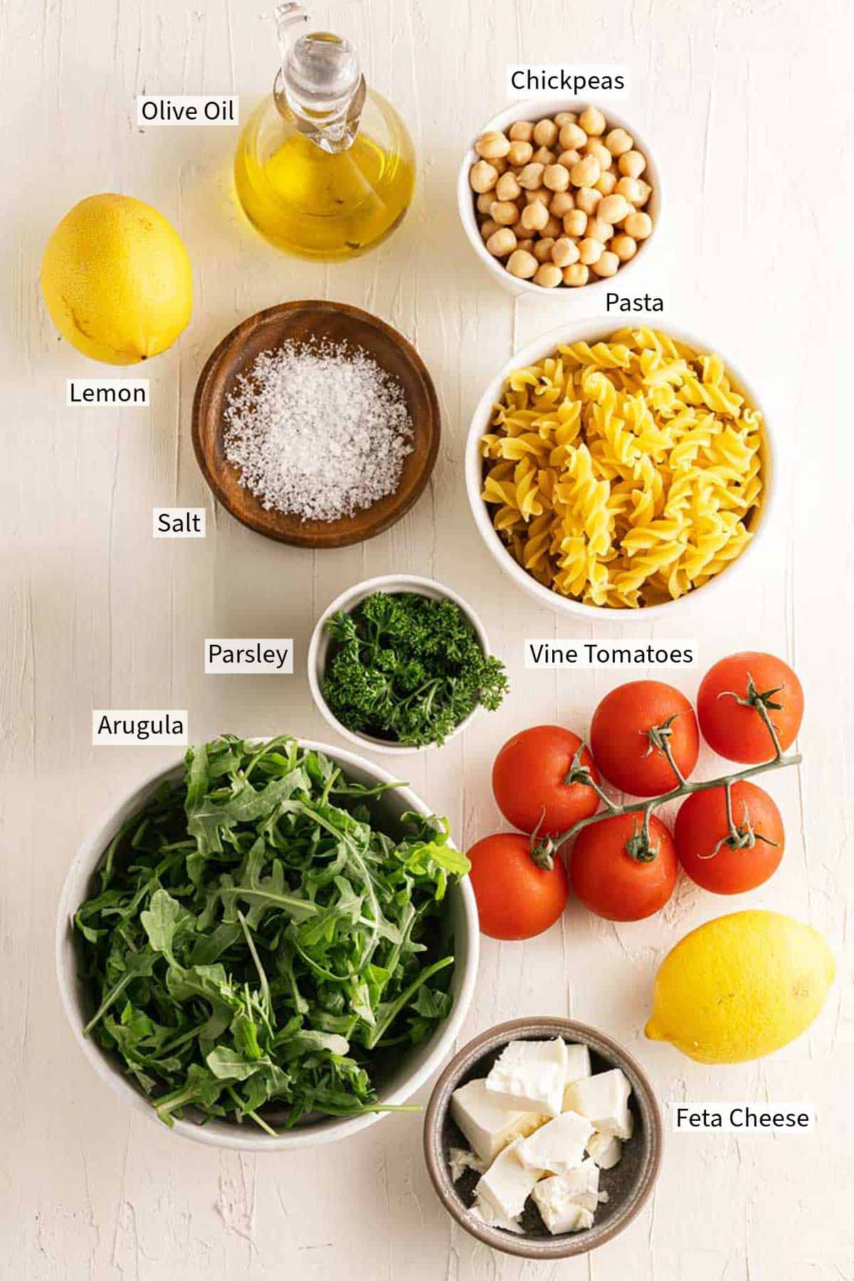 Fresh ingredients arranged on a table, labeled for a mediterranean-style Chickpea Pasta Salad.