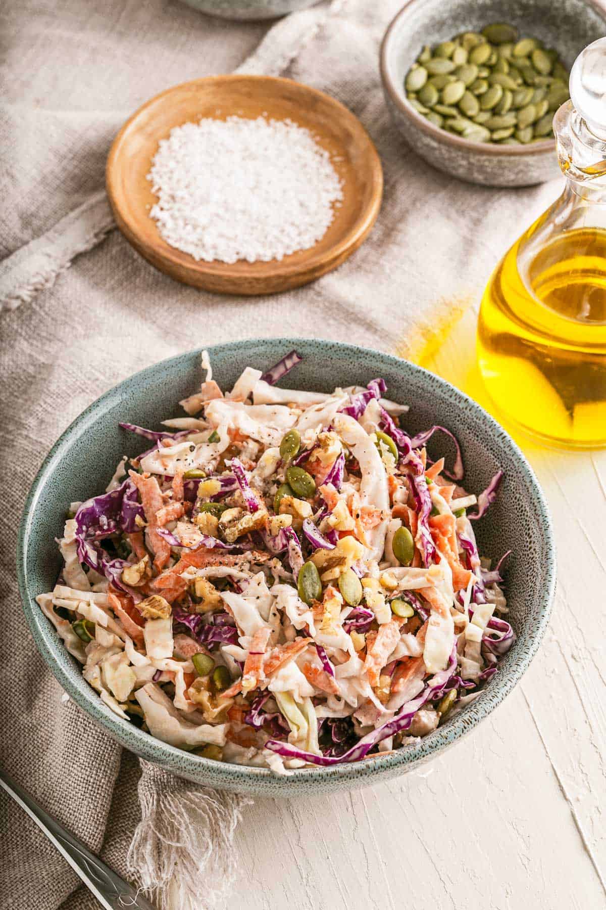 Bowl of crunchy coleslaw on a table surrounded by ingredients.