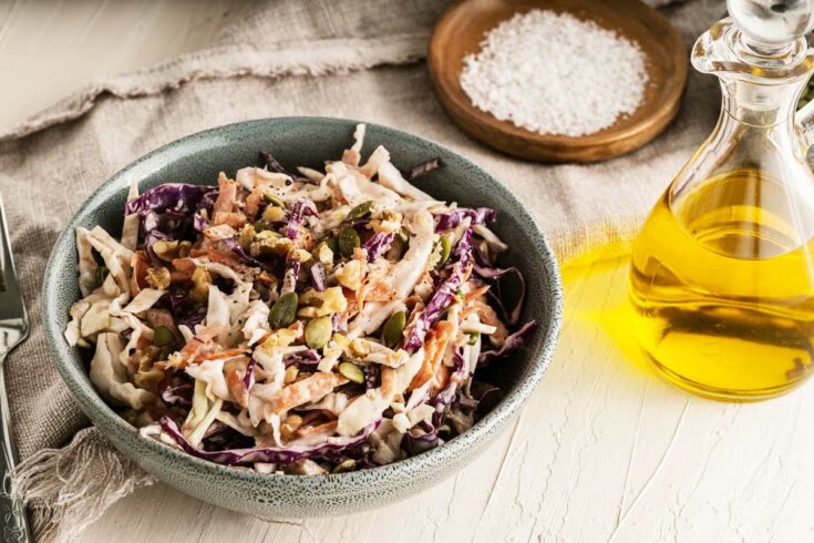 Bowl of coleslaw with bottle of olive oil.