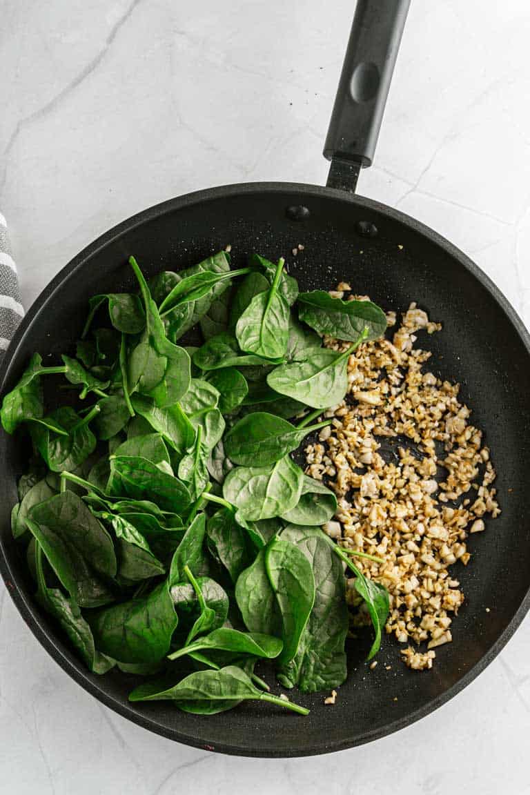 Frying pan with suateed mushrooms and fresh spinach.