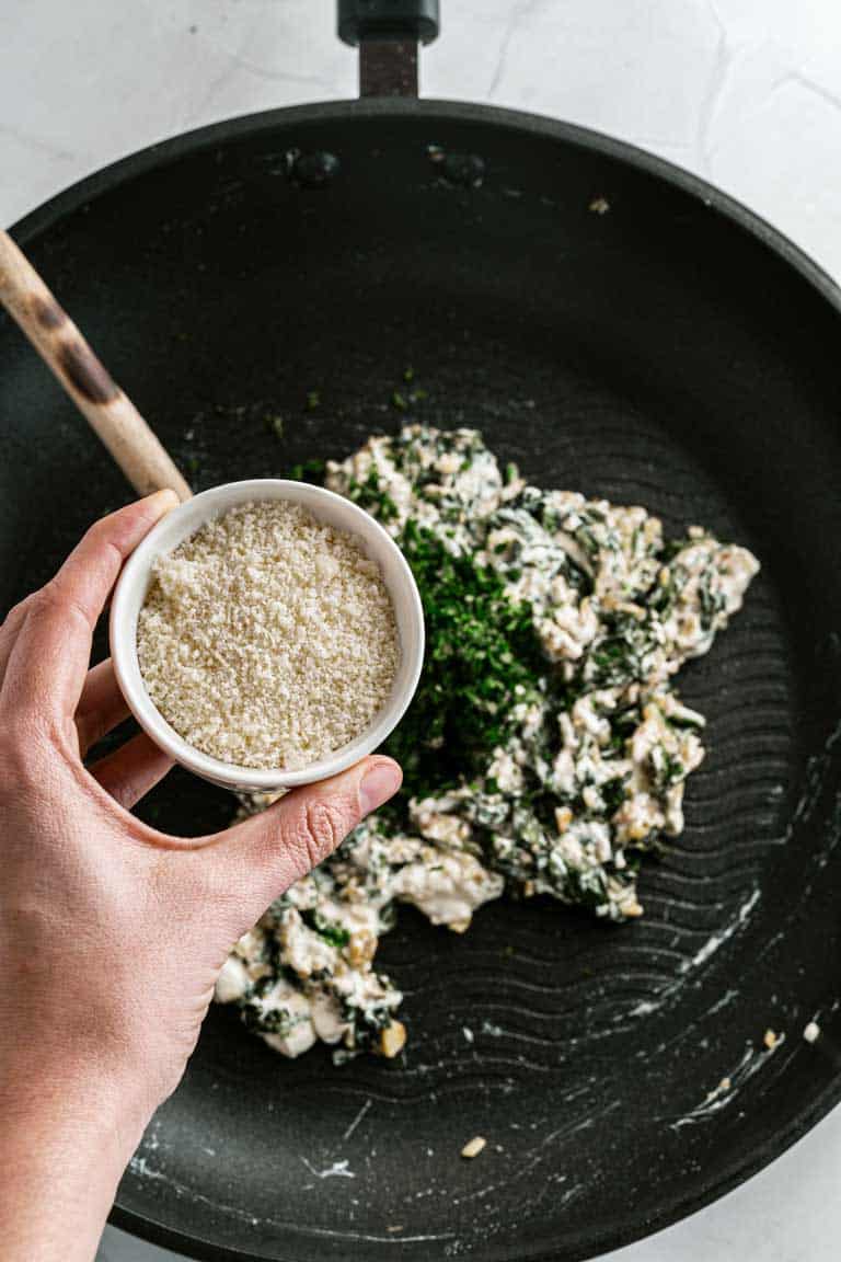 Close up of hand pouring parmesan into a stuffed mushroom mix in a pan.