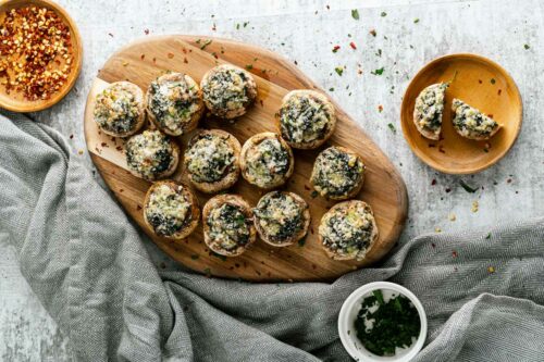 Wooden platter of cooked stuffed mushrooms.