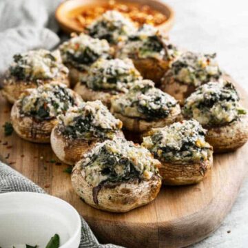 Stuffed mushrooms with spinach and parmesan cheese on a wooden cutting board.