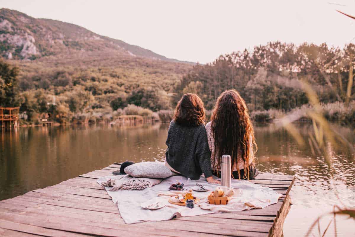 two girls having a picnic in autumn on a dock by a lake. 