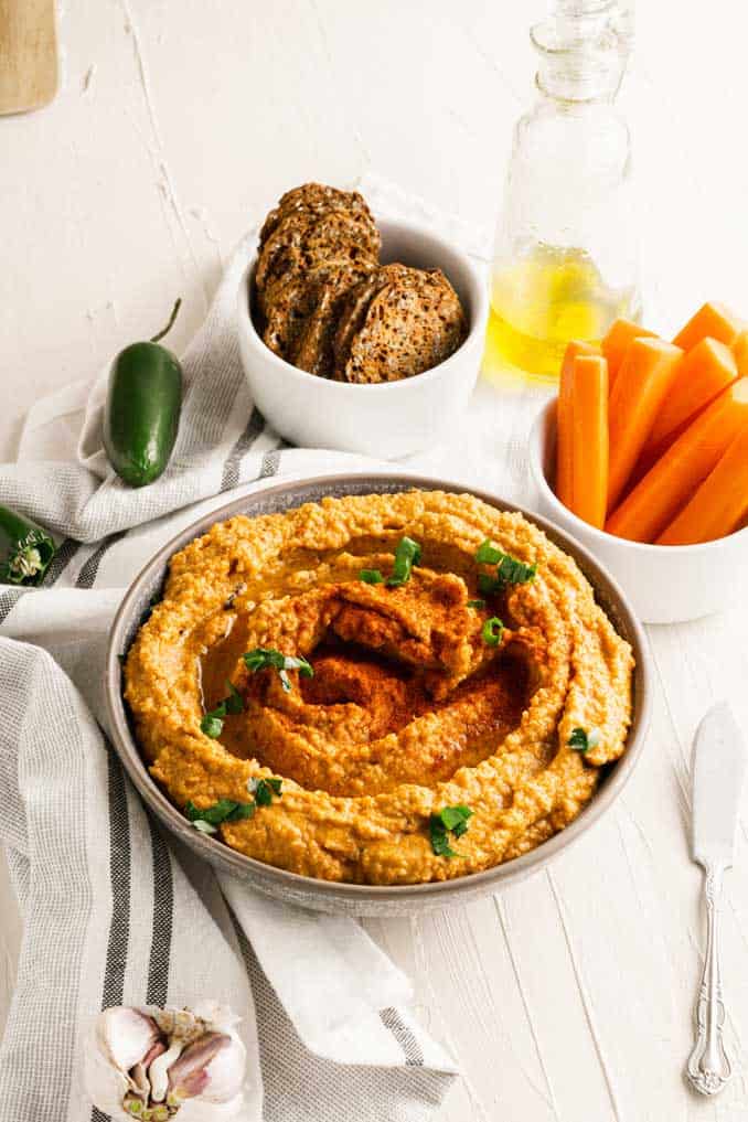 Bowl of roasted red pepper hummus with chipotle with bread crisps and carrot sticks. 