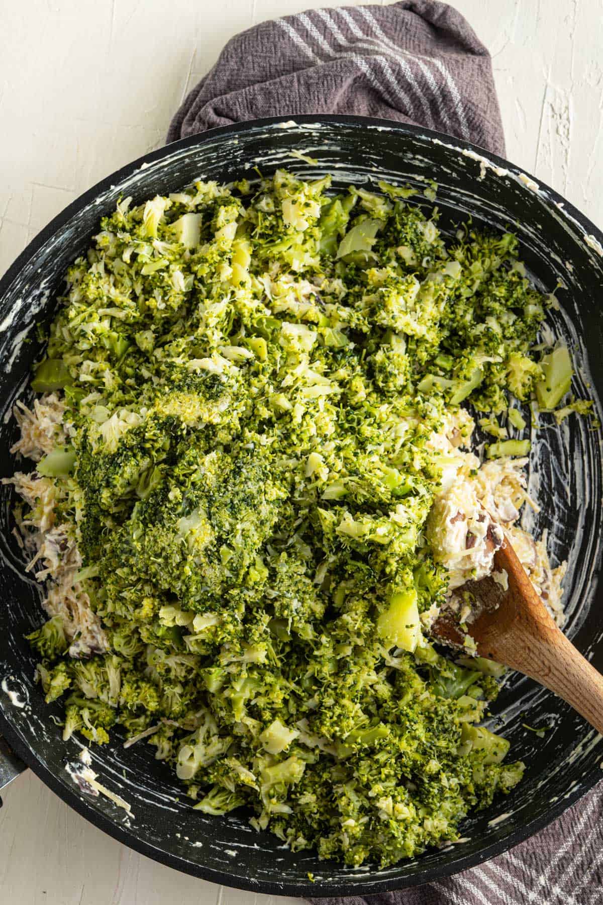 Mixing finely chopped broccoli with cheese in a pan.