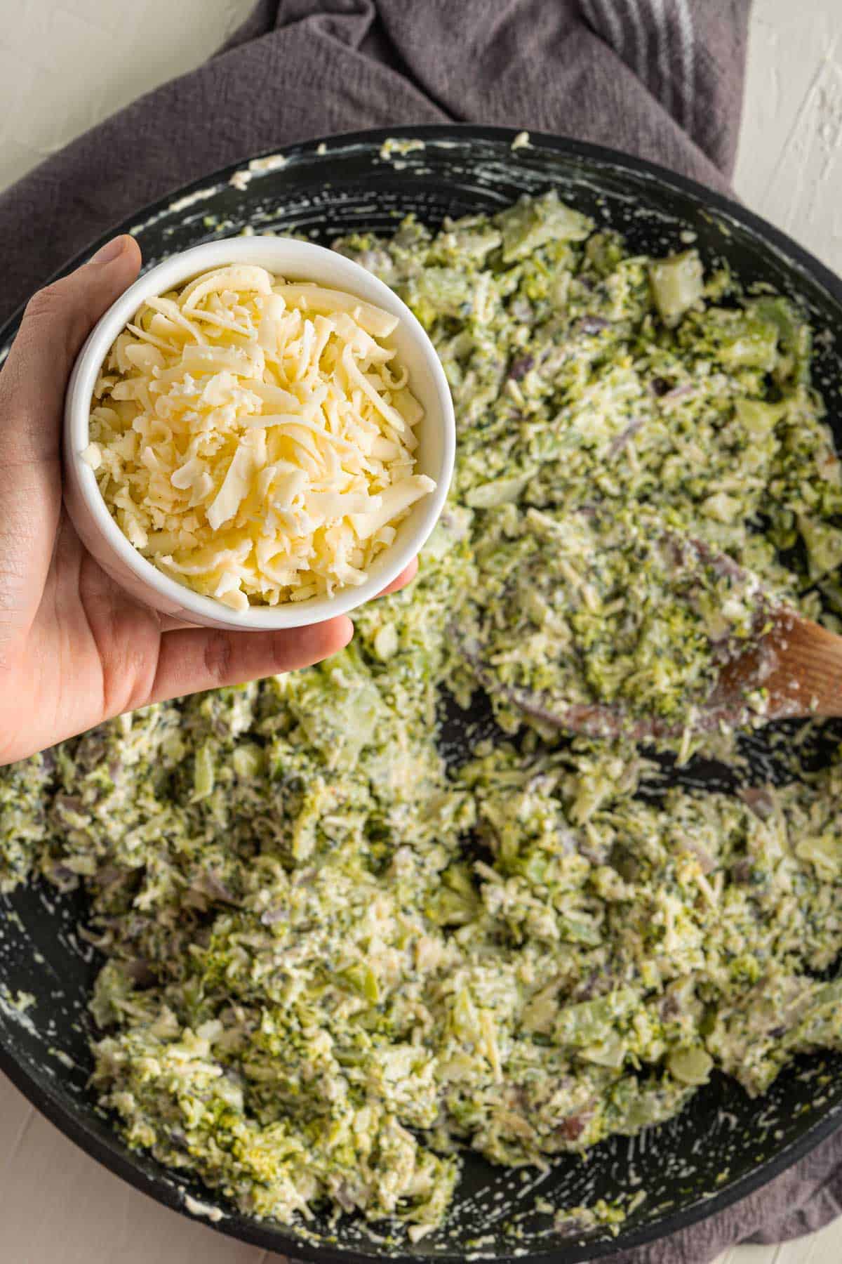 Pouring grated cheese into a pan with broccoli for dip.