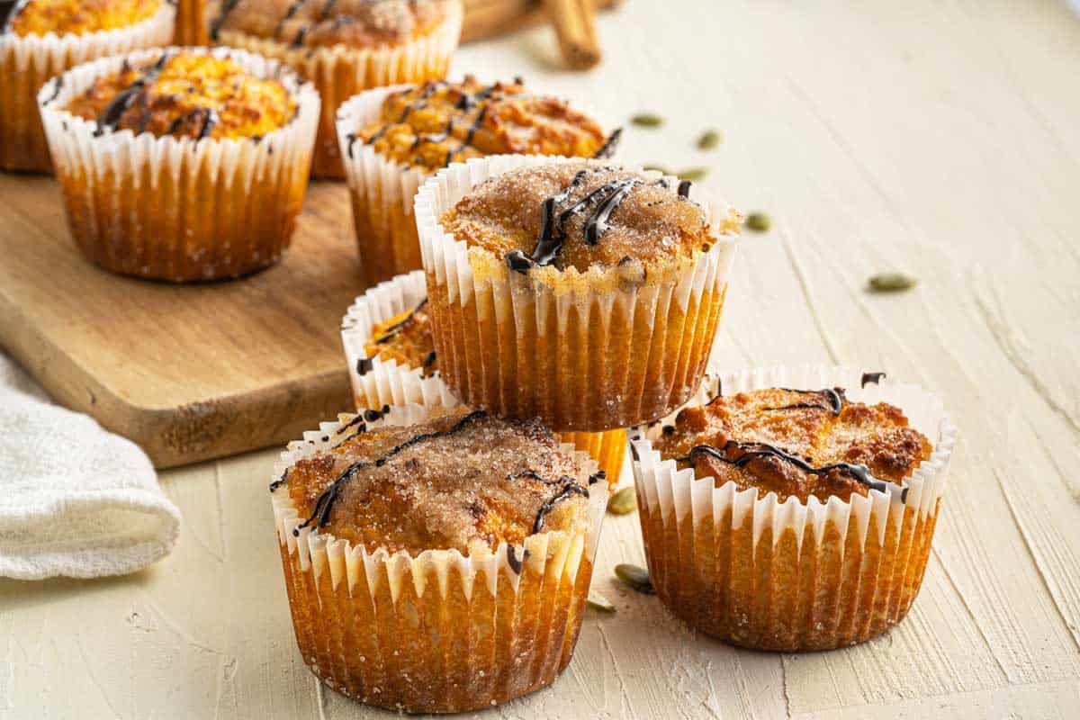 Freshly baked pumpkin muffins on a wooden board with sugar sprinkled on top.