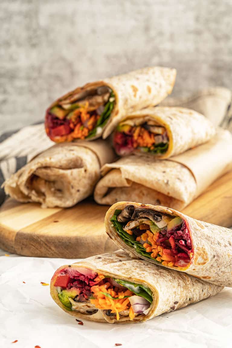 Stacks of raw veggie wraps cut in half showing the fillings. 