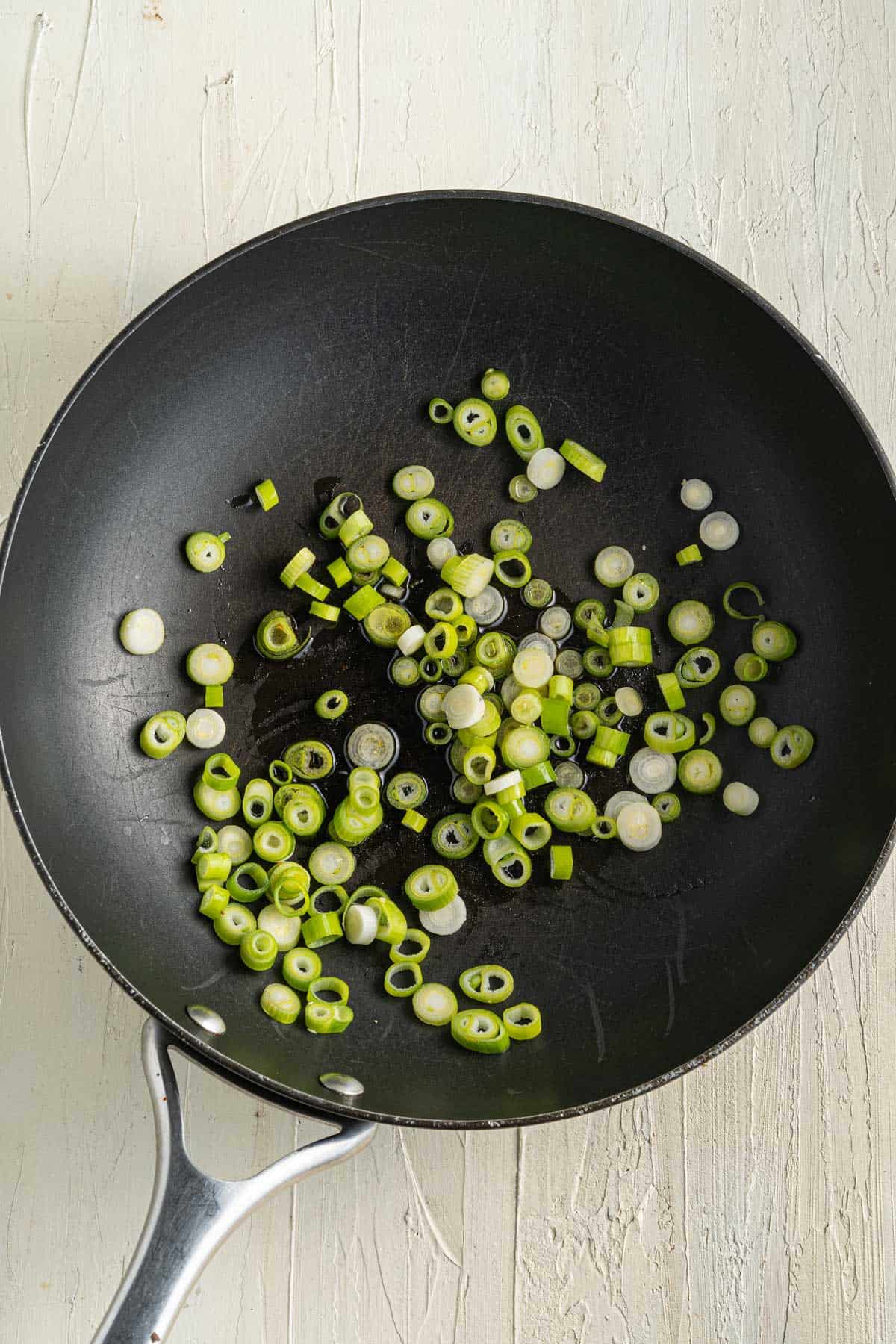 A black frying pan containing chopped green onions on a light-colored surface.
