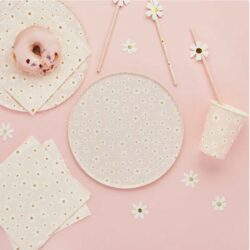 A pink-themed picnic paper tableware featuring a donut on a plate, a paper cup, napkins, straws with daisy decorations, and a daisy-patterned plate on a pink surface.