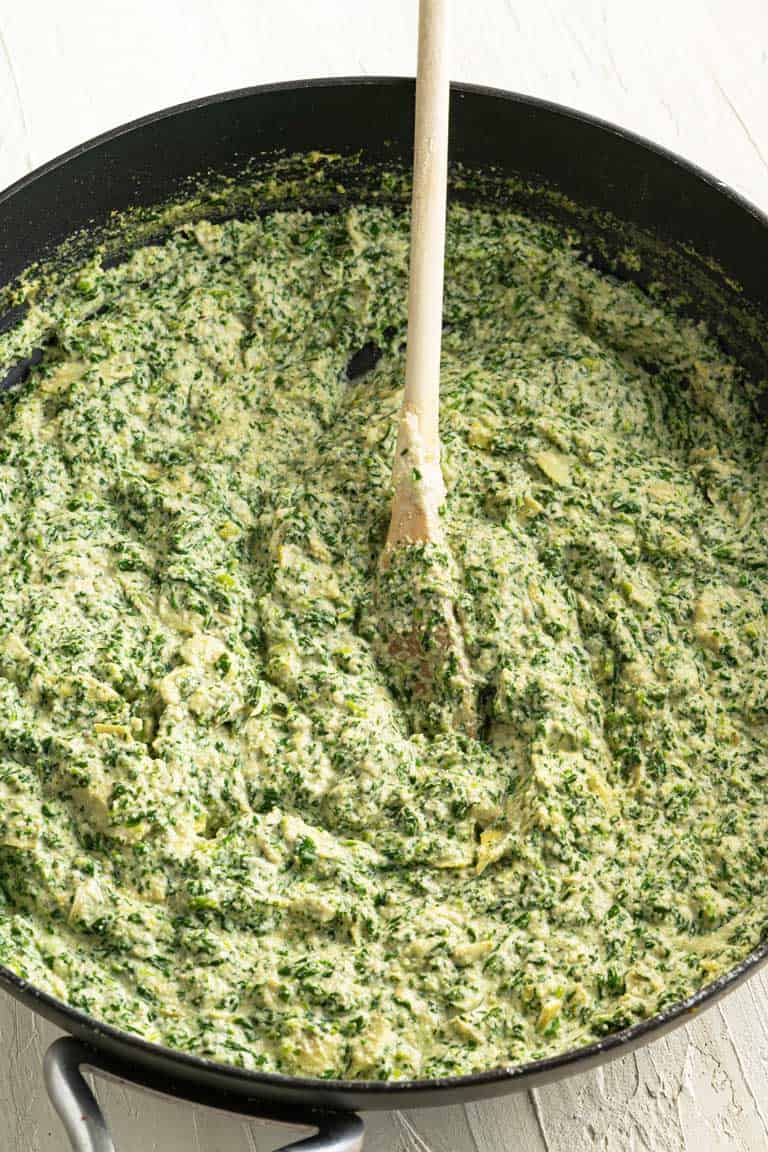 Vegan spinach and artichoke dip being mixed in a skillet over a stove top.
