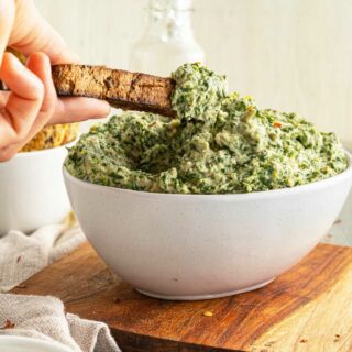 Dipping a toast stick into a bowl of artichoke and spinach dip.