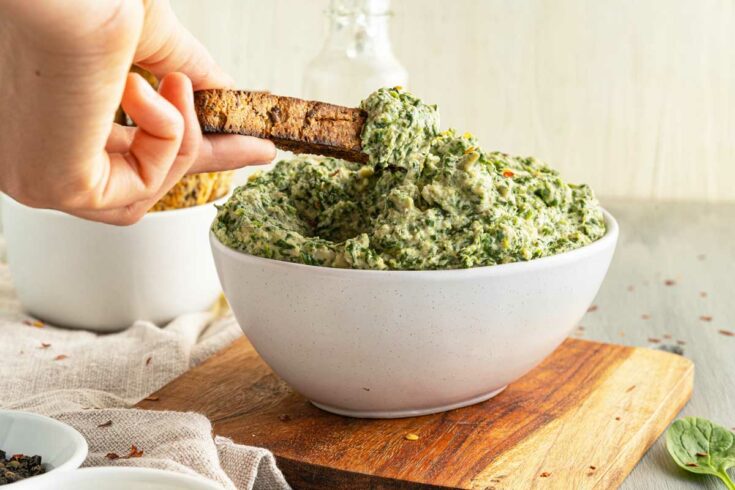 Dipping a toast stick into a bowl of artichoke and spinach dip.