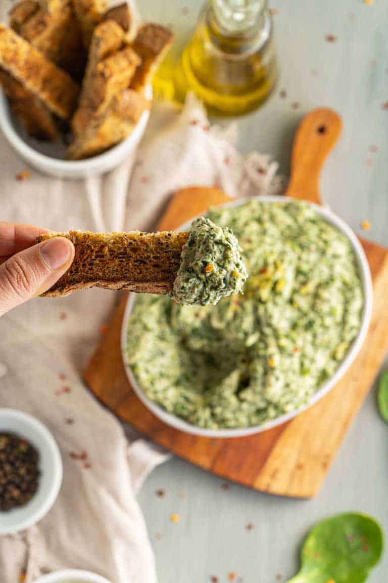 Holding a toast finger with spinach and artichoke dip on it.