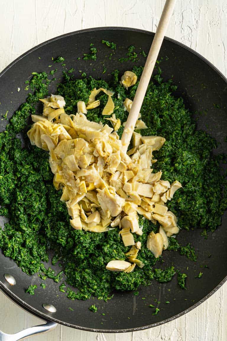 Chopped artichoke hearts and frozen spinach being sauteed in a pan.