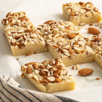 Squares of white chocolate fudge with almonds on baking paper.
