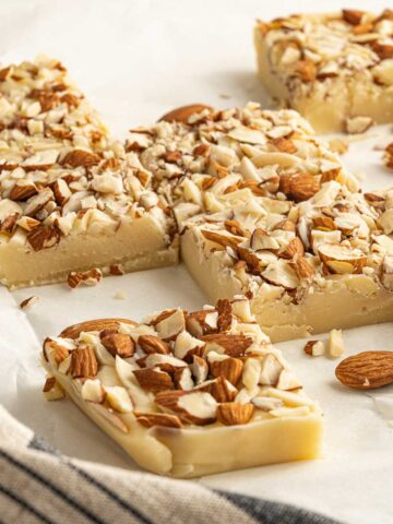 Squares of white chocolate fudge with almonds on baking paper.