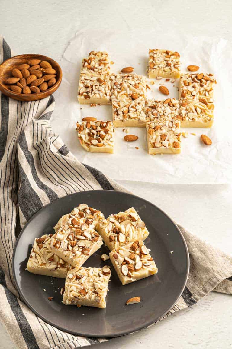 Squares of white chocolate fudge with almonds on a plate and on baking paper. 