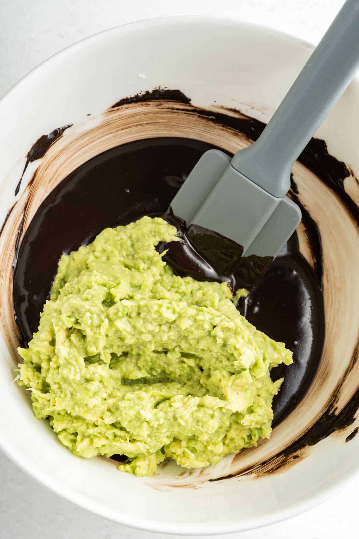Mashed avocado and melted chocolate in a bowl with a rubber spatular. 