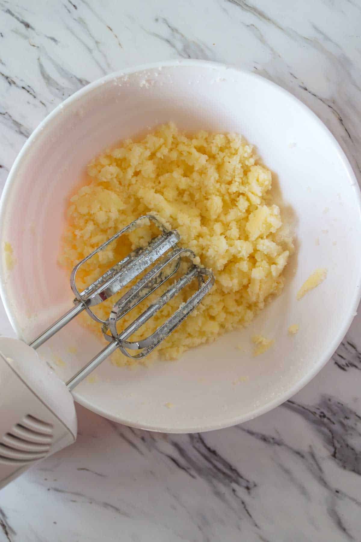 A white bowl with creamed butter and sugar and beaters.