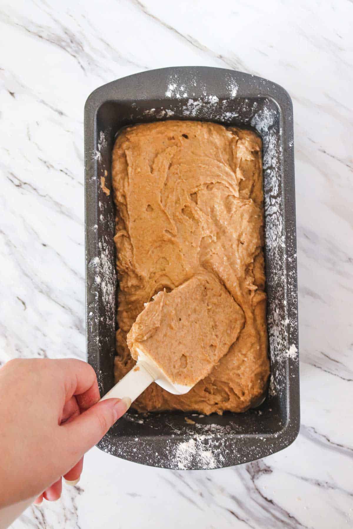 A person using a spatula to stir the gingerbread batter in a baking pan.