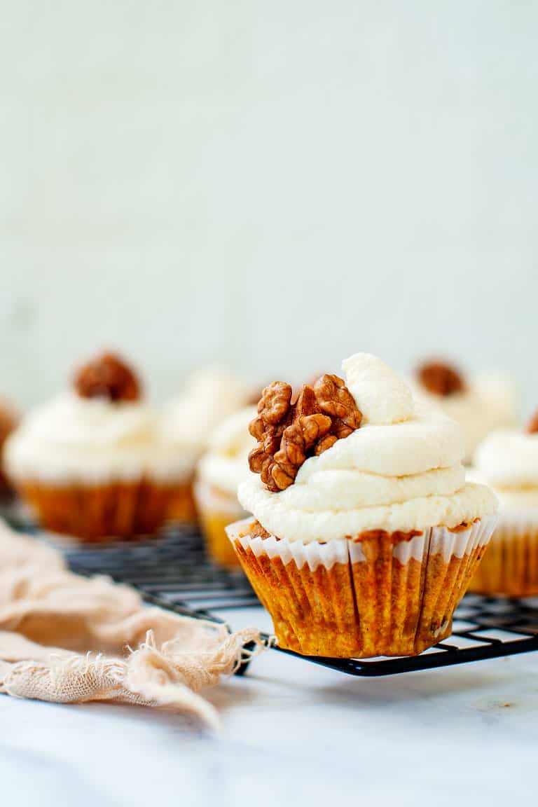 A carrot cake cupcake with cream cheese frosting topped with a walnut. 