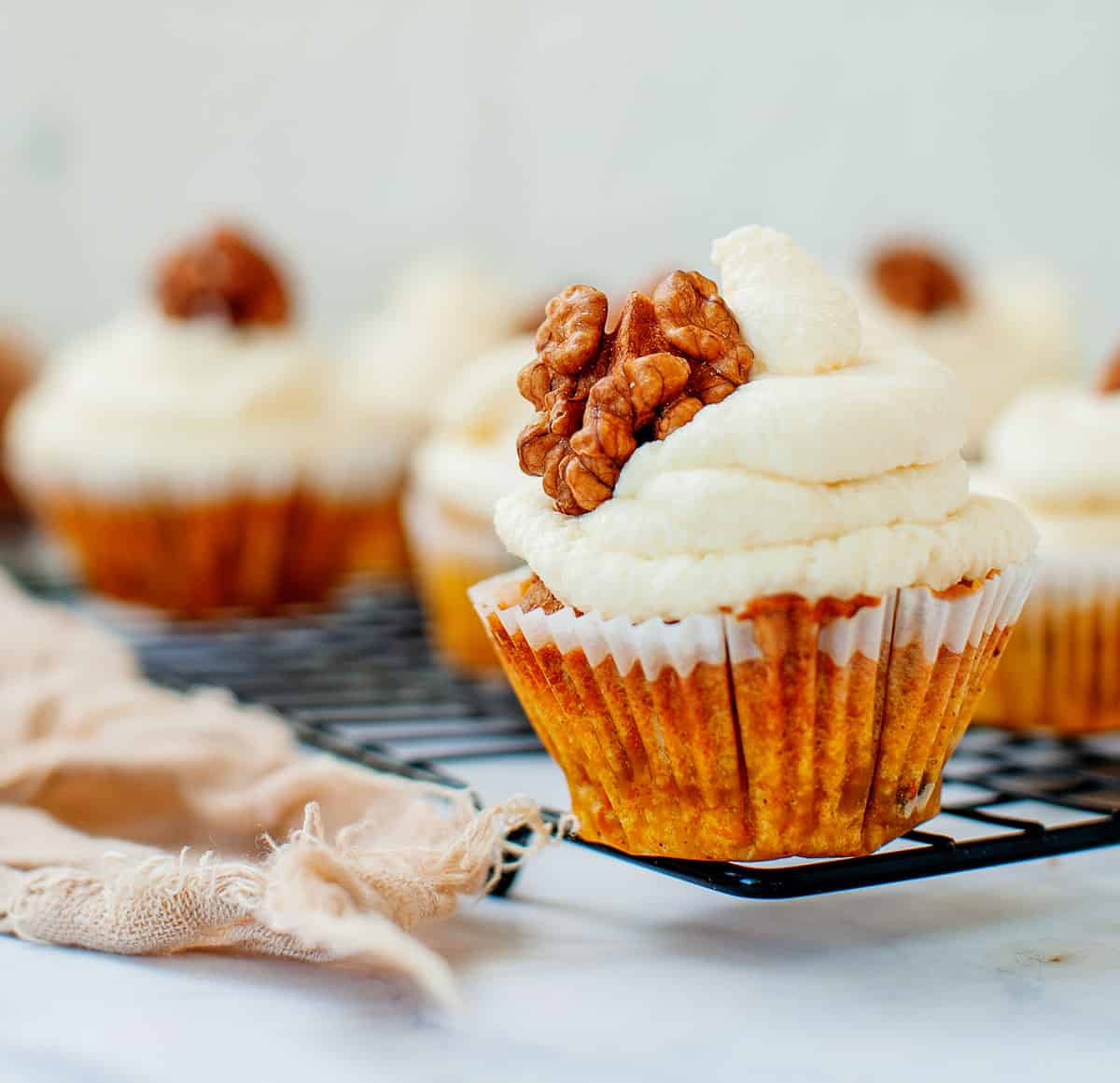 A carrot cake cupcake with cream cheese frosting topped with a walnut.