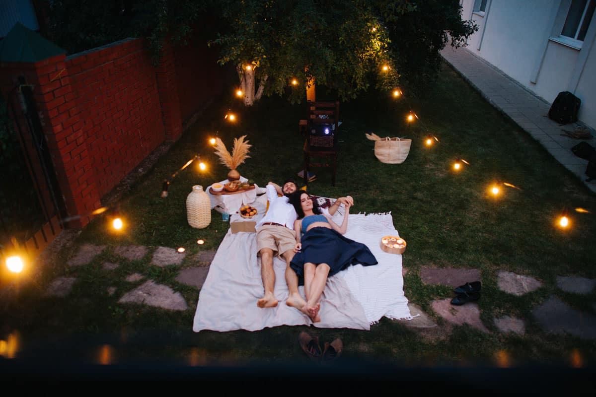 Couple lying on a blanket in the backyard at night enjoying a romantic night picnic. 