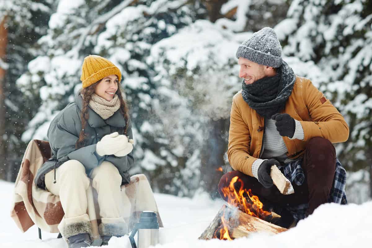 Couple enjoying a romantic winter picnic in the snow in front of a fire. 