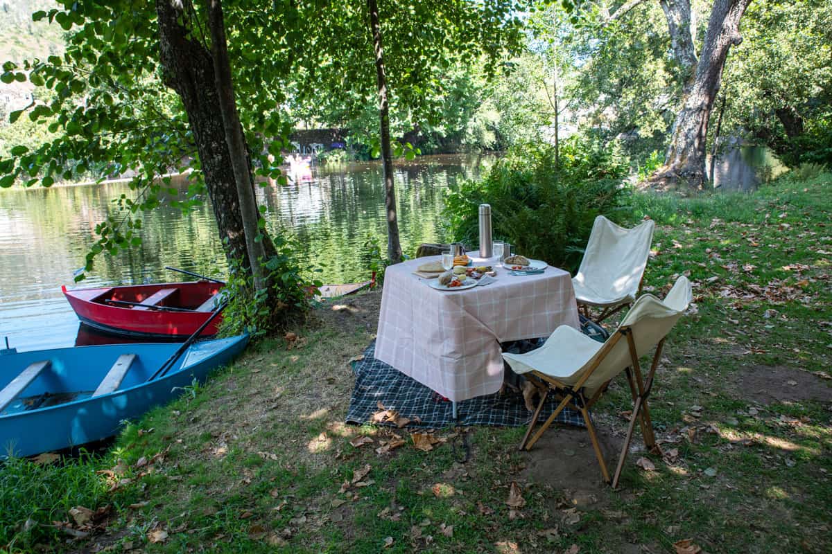 Una escena de picnic romántico junto a un río con coloridos botes de remos. 