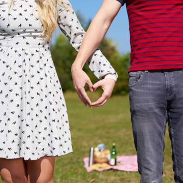 Valentines couple making heart shape with their hands in front of a picnic.