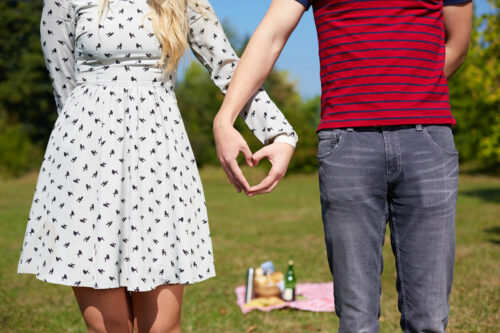Valentines couple making heart shape with their hands in front of a picnic.