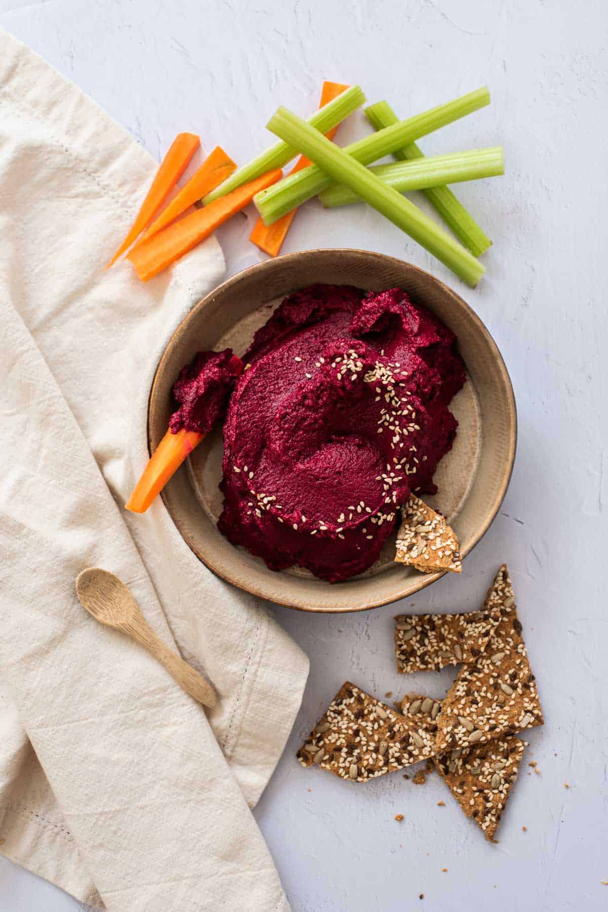 A bowl of beet hummus served with carrots, celery, and crackers for a delicious and healthy snack.