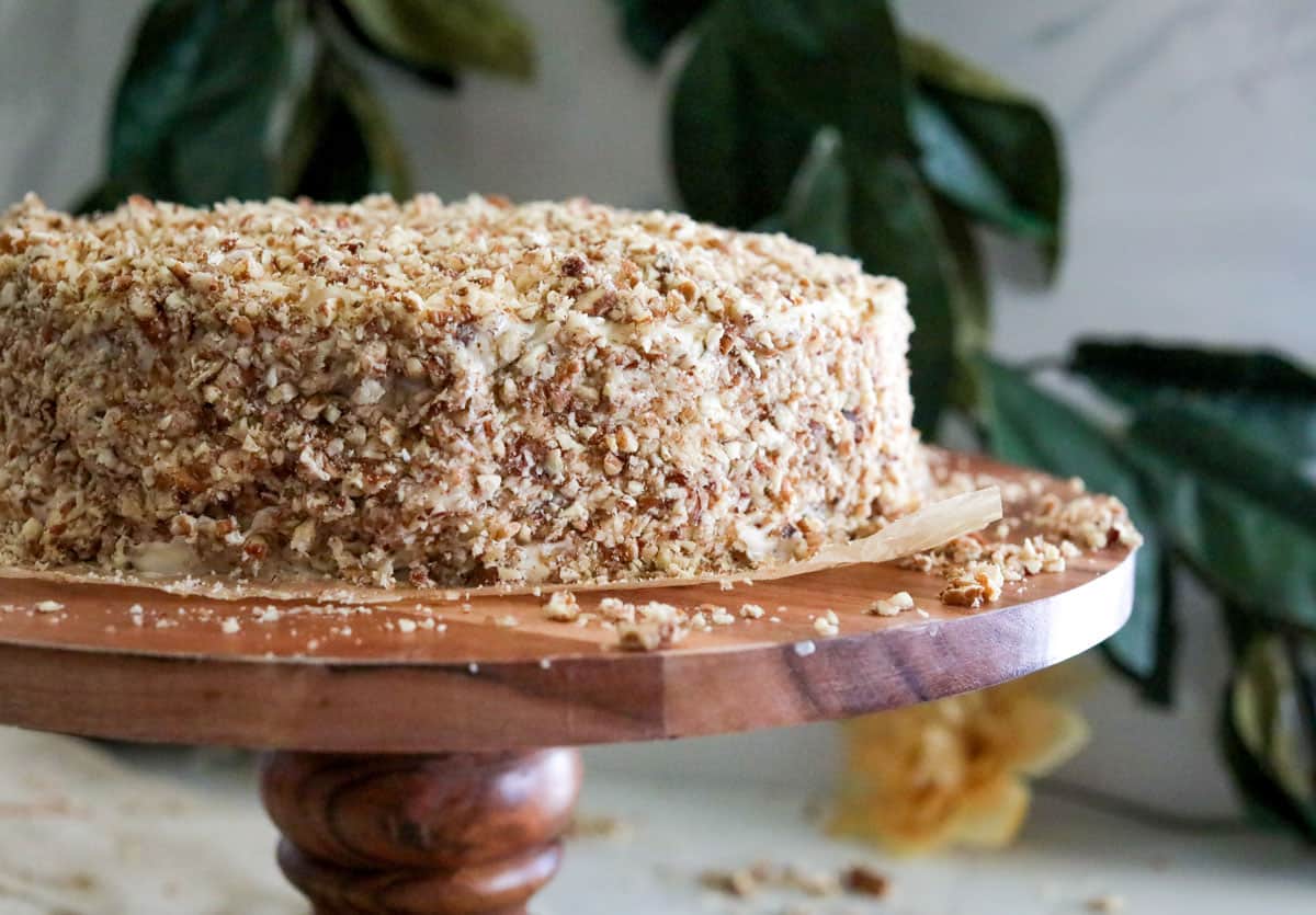 A hummingbird caked covered in crushed pecans on a wooden cake stand.