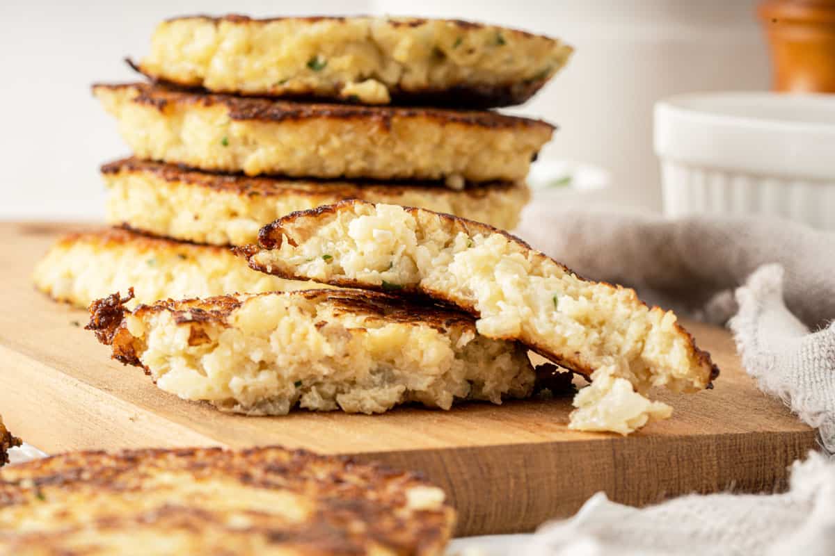 A stack of Cauliflower hash browns on a wooden board. 
