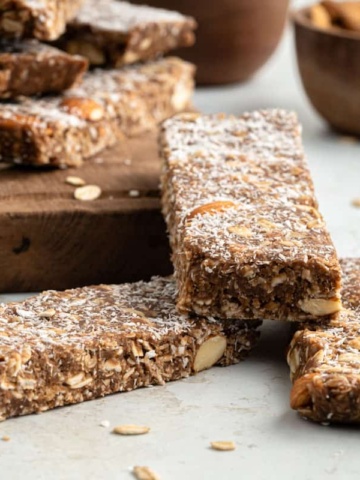 Homemade chocolate granola bars stacked on a wooden board sprinkled with coconut.
