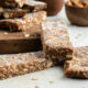 Homemade chocolate granola bars stacked on a wooden board sprinkled with coconut.