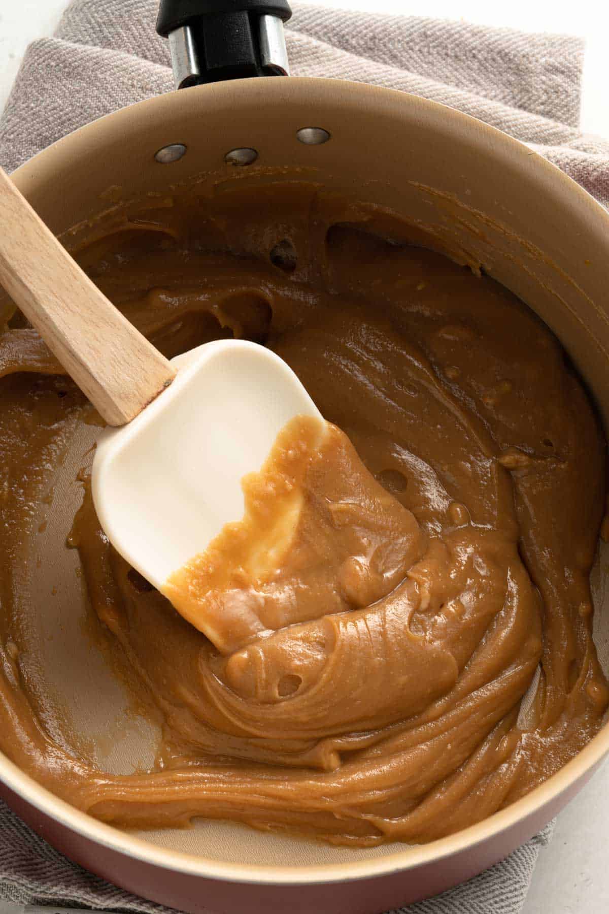 Strirring Maple syrup and nut butter in a saucepan with a rubber spatula.