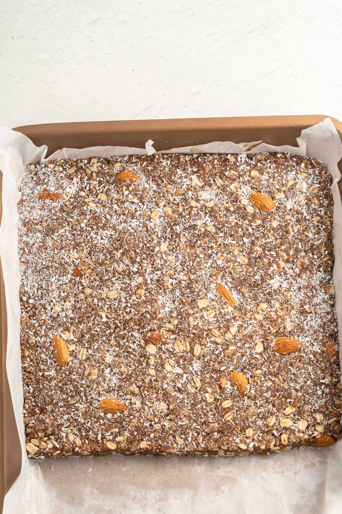 Choloate oat bar mix in a pan lined with parchment paper ready for setting in the fridge.