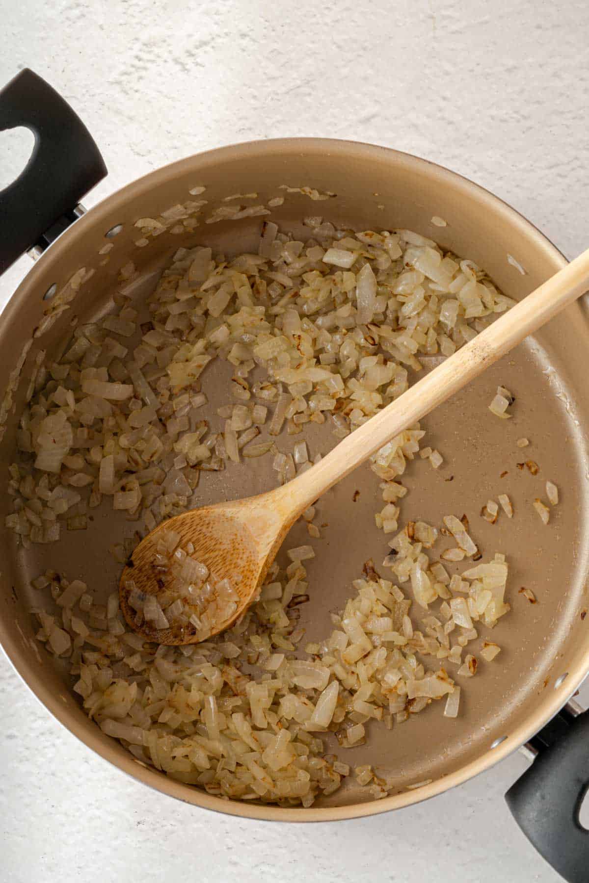Sauteing onions in a pan with a wooden spoon.