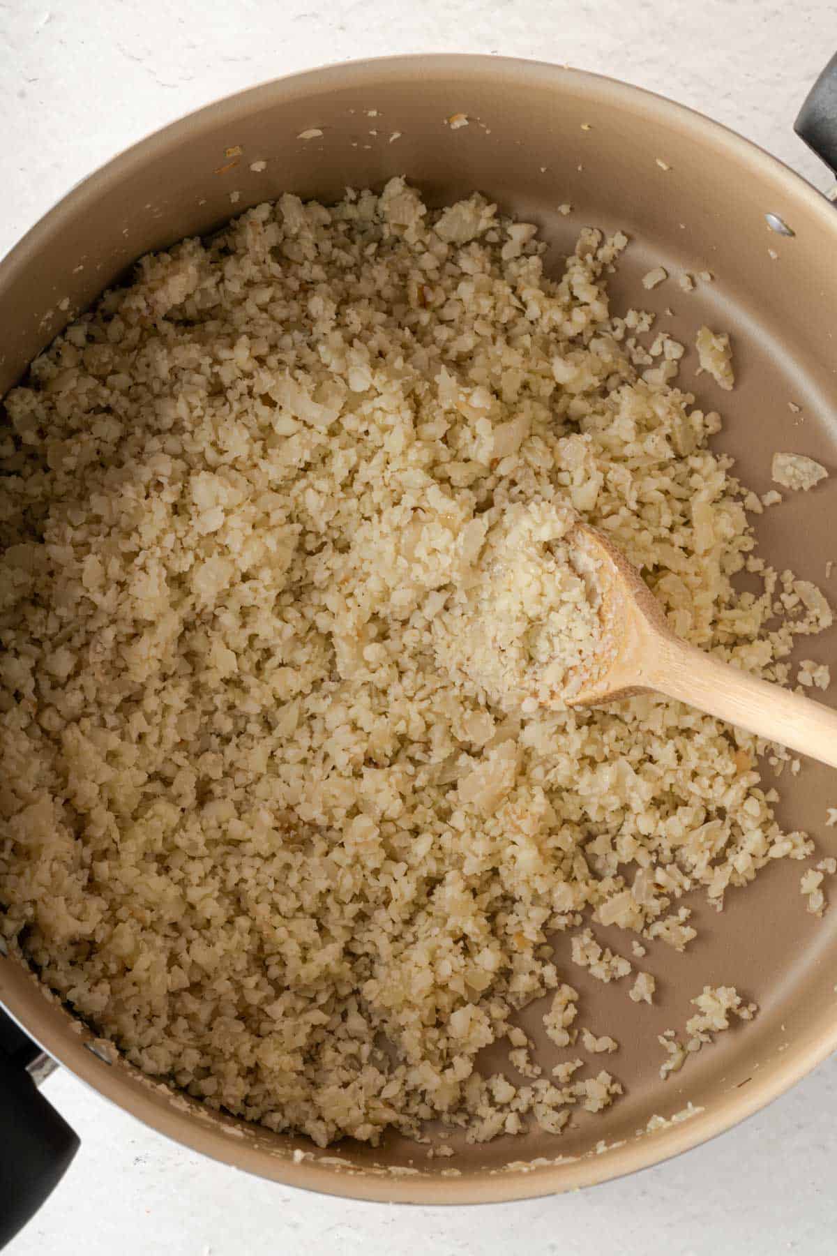 Cauliflower rice in a pan with a wooden spoon.