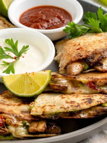 A plate of freshly cooked mushroom quesadillas with dipping sauces.