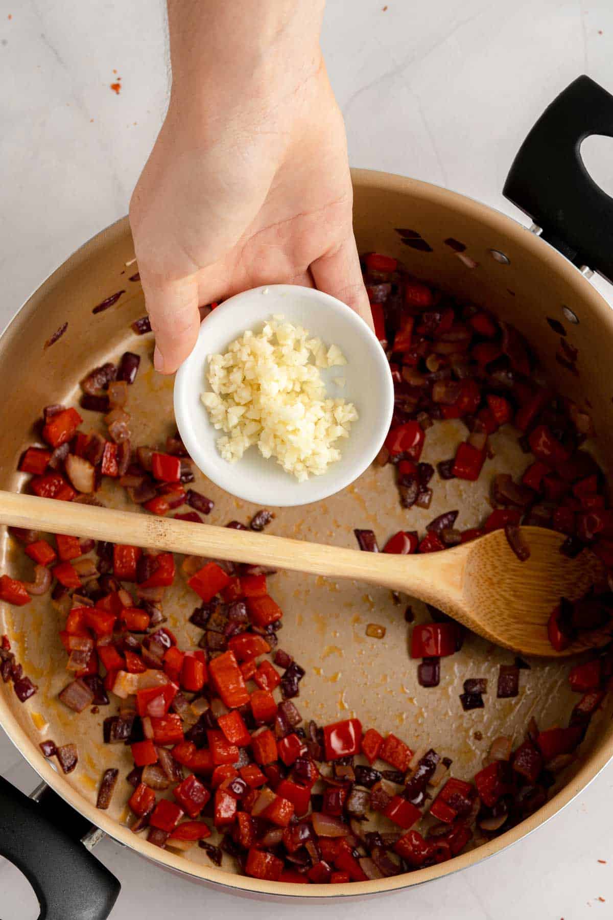 Adding garlic to a sauteed mix of onions and red peppers.