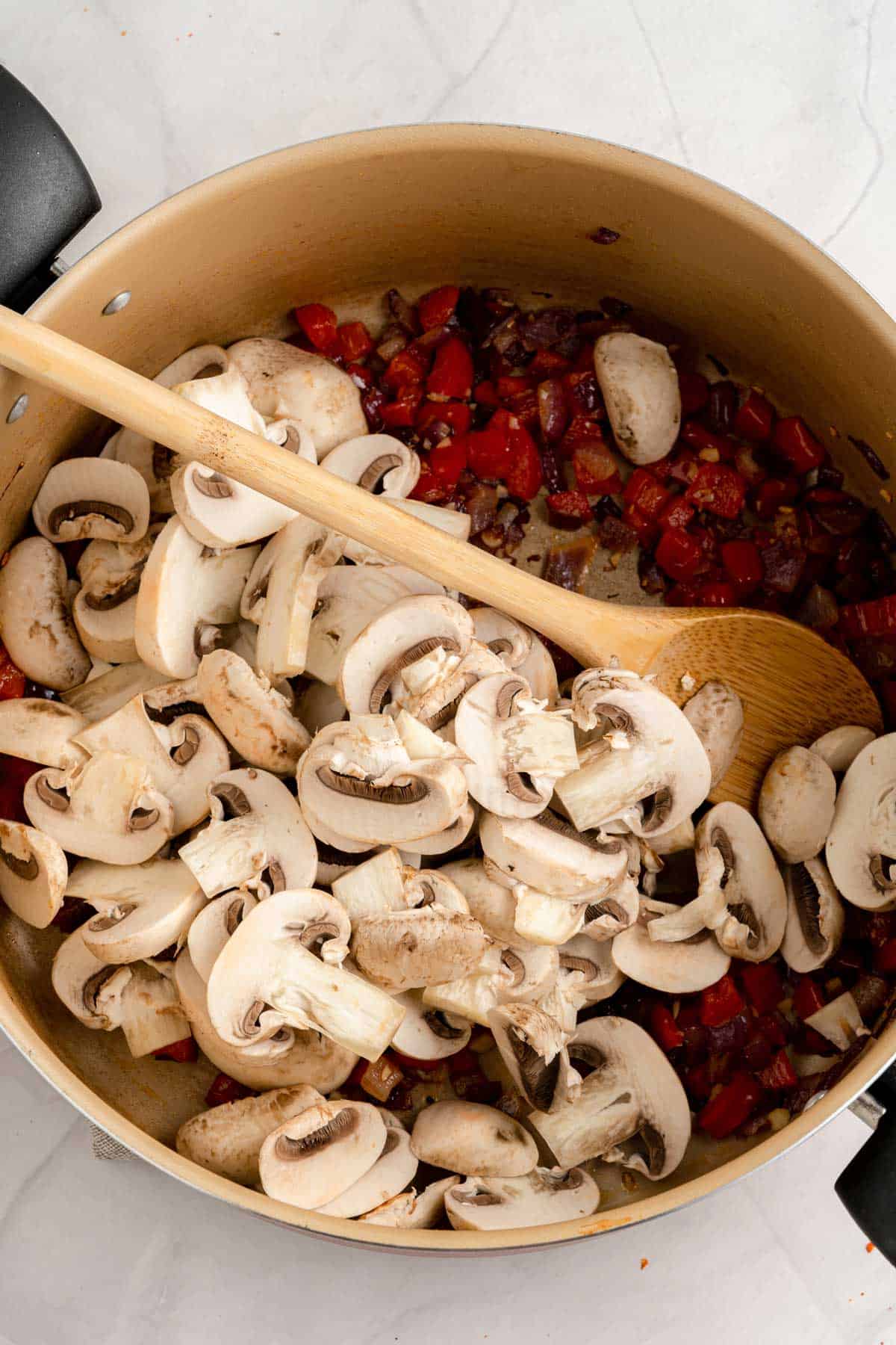 Adding mushrooms to a sauteed mix of onions and red peppers.