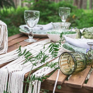 Boho table setting for a picnic with macrame decoration and green foliage