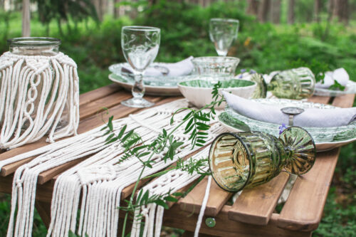 Boho table setting for a picnic with macrame decoration and green foliage